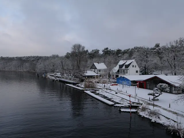 The image shows a picturesque winter scene of a small town next to a body of water, with...