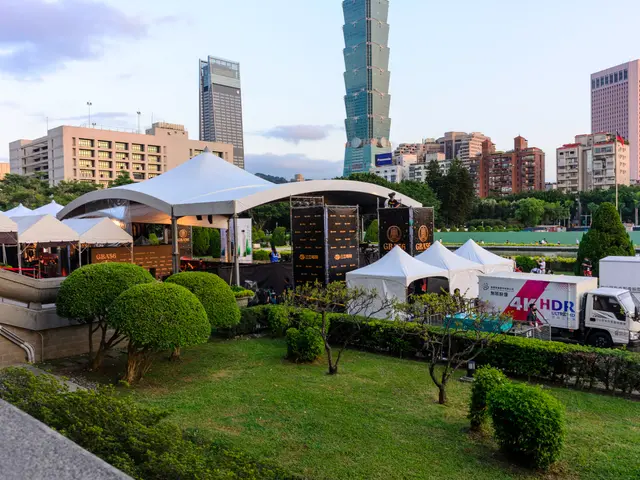 The image shows a group of tents set up in the middle of a park, surrounded by lush green grass,...
