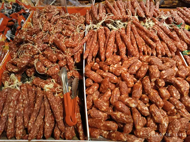 The image shows a market with a display case filled with lots of different types of sausages, as...