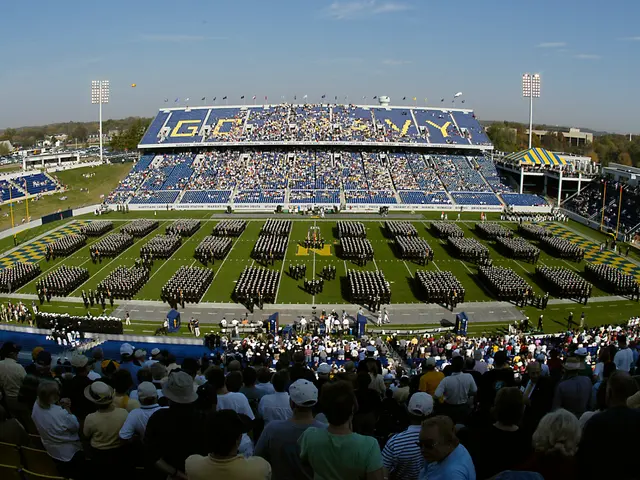 The image shows a large crowd of people watching a football game in a stadium. The stadium is...