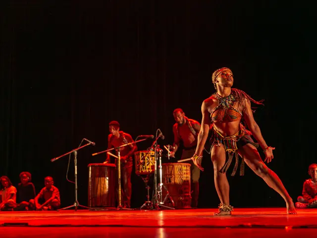 The image shows a woman in a bikini dancing on a stage surrounded by a group of people sitting on...