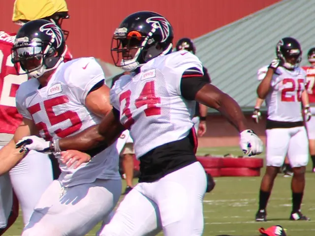 The image shows a group of men playing football on a field, with a wall in the background. All of...