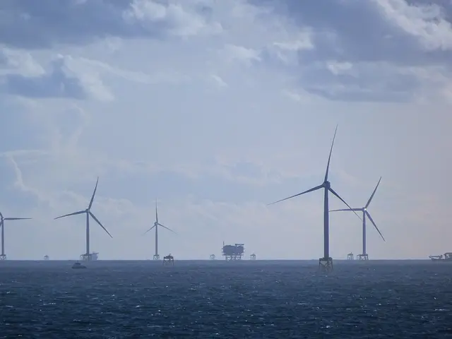 The image shows a large group of wind turbines in the ocean, with boats in the foreground and a sky...