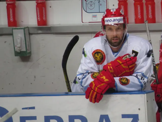 The image shows a hockey player sitting on the bench with his arms crossed, wearing a helmet and...