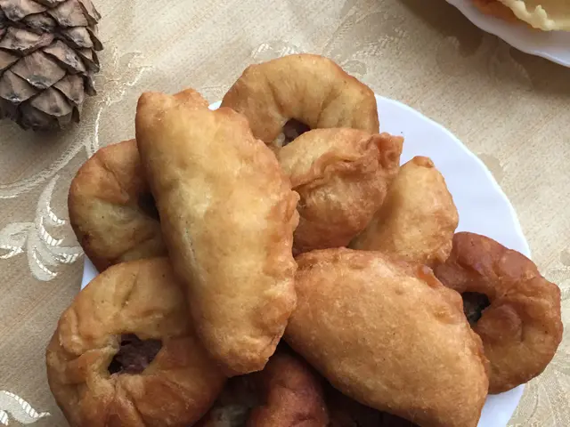 The image shows a white plate filled with fried doughnuts on top of a table, accompanied by a bowl...