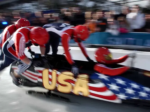 The image shows a group of bobsleds racing down a track in front of a crowd, with a blurred...