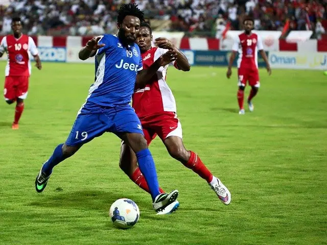 The image shows a group of men playing soccer on a field, with a crowd of spectators in the...