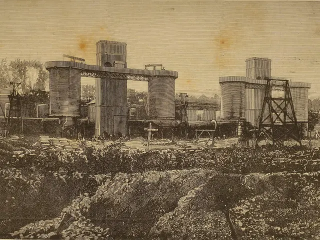The image shows an old black and white photo of a factory with a large building in the background,...