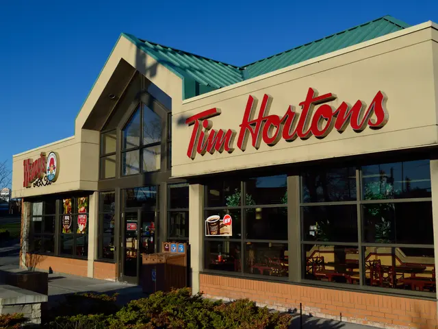 The image shows a Tim Hortons restaurant with glass walls and windows, text on the building, plants...