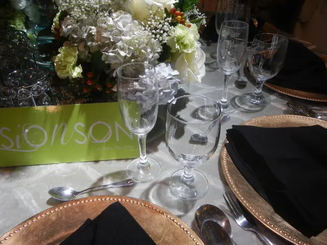 The image shows a table set for a formal dinner with gold chargers, black napkins, spoons, forks,...