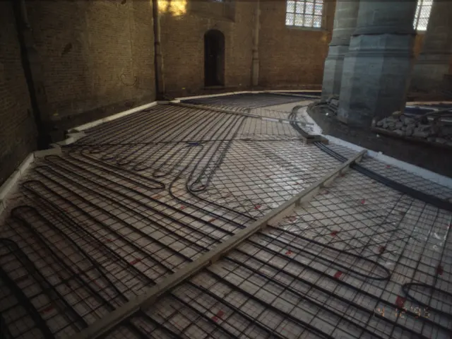 The image shows a room with a floor heating system in the middle of it, surrounded by iron grills,...