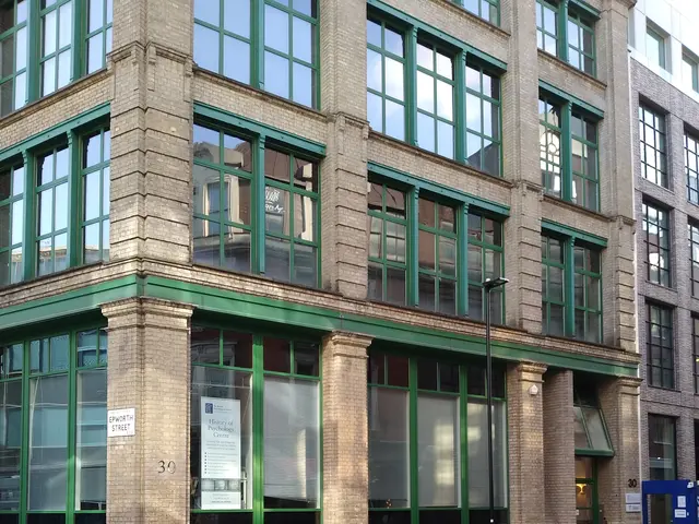 The image shows a large building with many windows on the side of it, situated on a road with a...