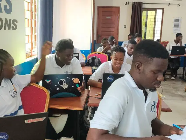 The image shows a group of people sitting at desks in a classroom, with laptops, books, bags, and...