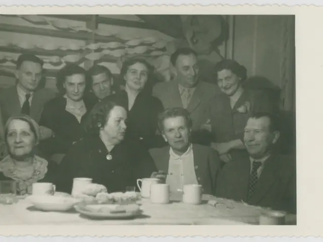 The image shows a group of people sitting around a table, smiling and enjoying each other's...