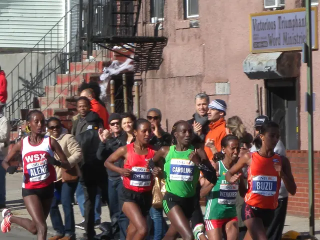 The image shows a group of women running in a marathon on a road surrounded by a crowd of people...