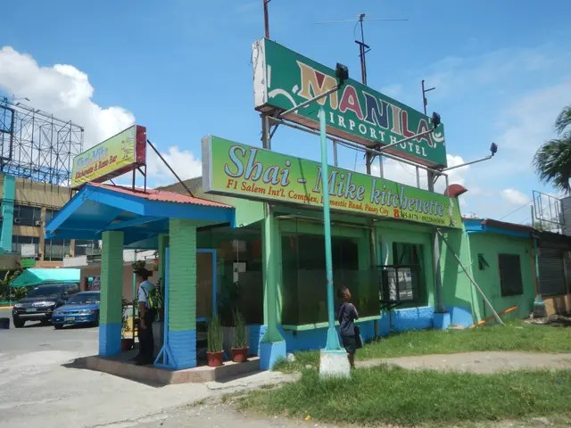 The image shows a bustling cityscape with buildings, motor vehicles on the road, persons standing...