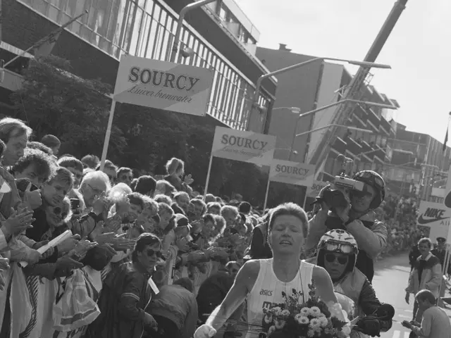 The image shows a woman crossing the finish line of a race, holding a bouquet of flowers in her...