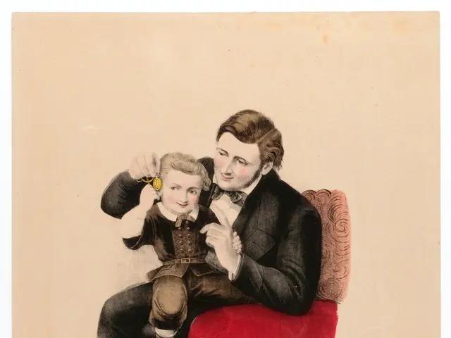 The image shows a man sitting on a red chair, holding a small child in his arms. The man has a warm...