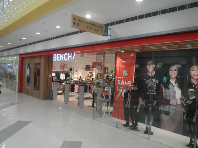 The image shows the inside of a shopping mall with mannequins in the window, clothes hung on...