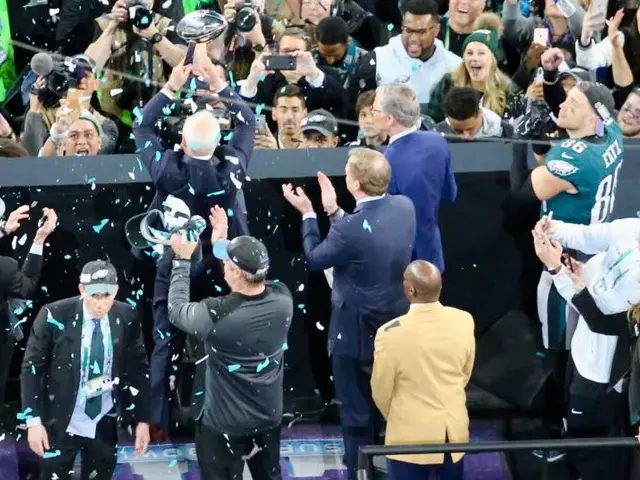 The image shows a group of Philadelphia Eagles players celebrating with the Vince Lombardi Trophy...