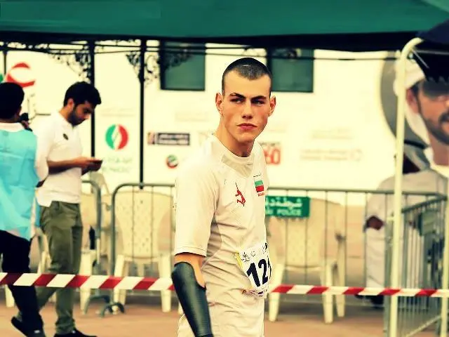 The image shows a man in a white shirt and red shorts running on a track, surrounded by a group of...