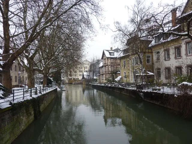 The image shows a picturesque winter scene of Strasbourg, France, with a river running through a...