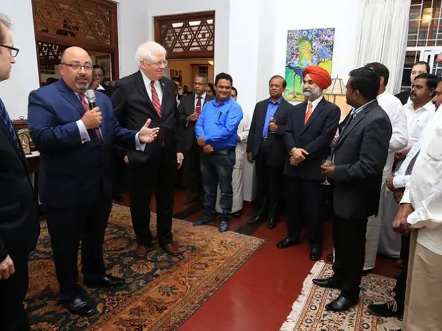 The image shows a group of men standing around each other in a room, with a man holding a...