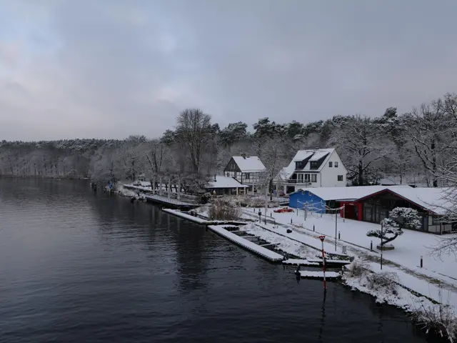 The image shows a picturesque winter scene of a small town next to a body of water, with...
