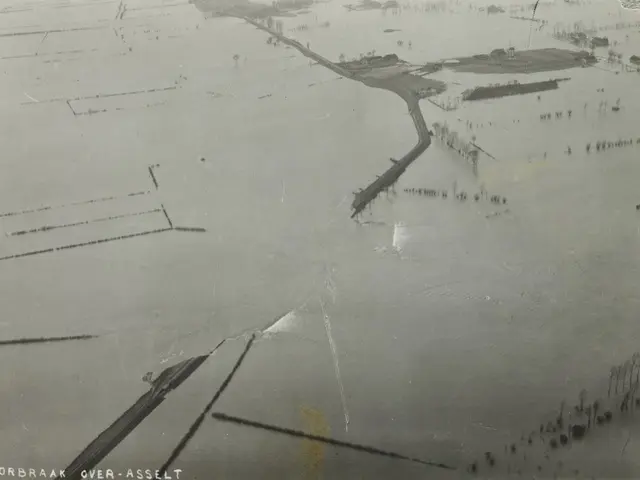 The image shows an aerial view of a flooded area with a road running through it. The photo is in...