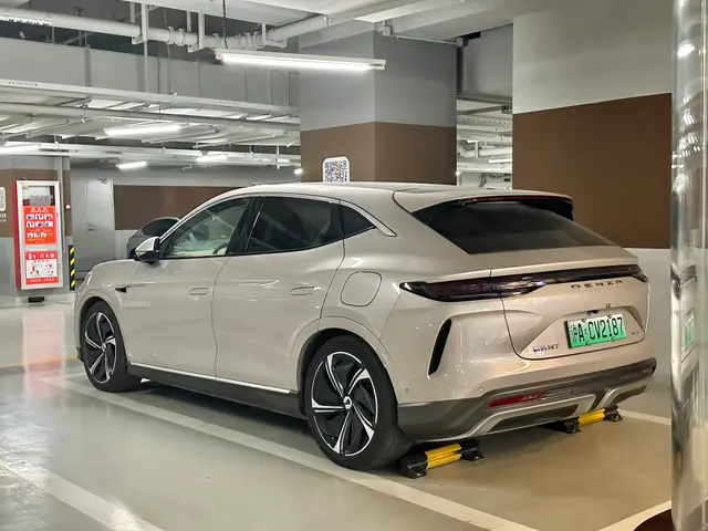 The image shows a white electric car parked in a parking garage, with a pillar on the right side...