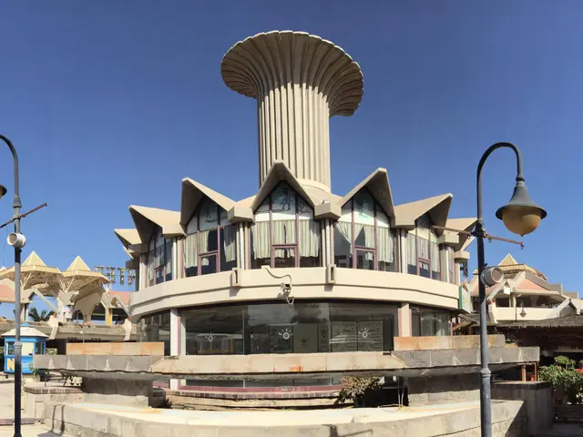 The image shows a city street with a fountain in the middle of it, surrounded by buildings, street...