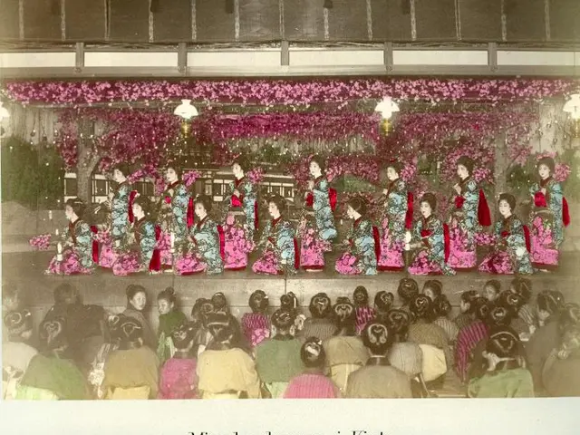 The image shows an old photo of a group of women in colorful kimonos sitting on a stage in front of...