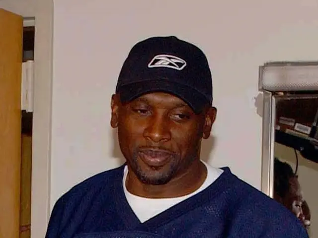 The image shows a man in a blue t-shirt and cap standing in front of a mirror, with a door on the...