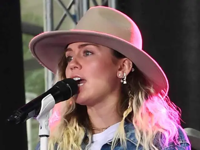 The image shows Miley Cyrus performing at the CMA Music Festival in Nashville, Tennessee. She is...