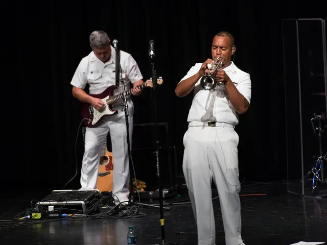 The image shows two men in white uniforms playing musical instruments on a stage. There are mics...