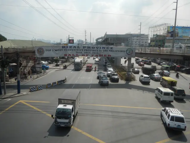 The image shows a busy street filled with lots of cars and trucks driving down it, with a bridge in...