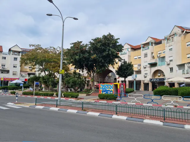 The image shows a city street with tall buildings in the background, street poles, street lights,...