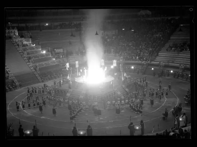 The image shows a black and white photo of a crowd of people in a stadium, illuminated by lights...