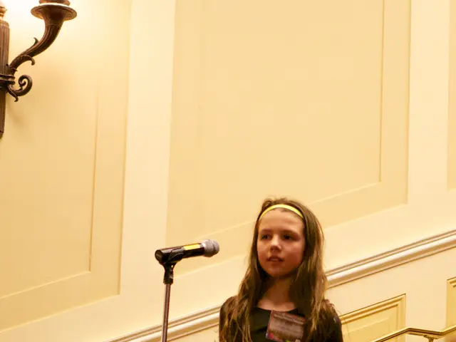 The image shows a young girl standing on top of a stage in front of a crowd of people, with a...
