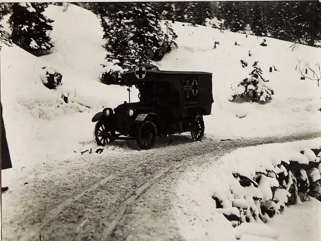 The image shows an old black and white photo of an ambulance driving down a snowy road, surrounded...