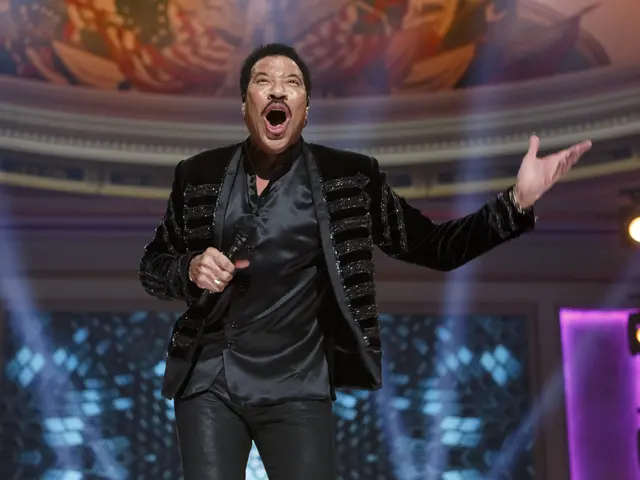 The image shows Lionel Richie performing at the Grammys, wearing a black dress and holding a...