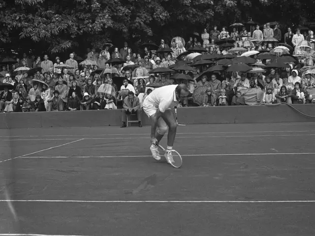 The image shows a man playing tennis on a court surrounded by a crowd of people, some of whom are...