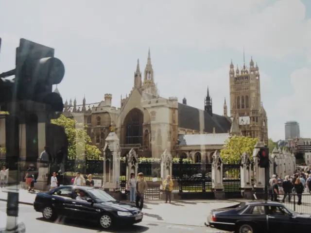 The image shows a bustling street scene with cars driving down the road, people walking on the...