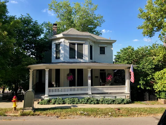 The image shows a white house with a flag on the front of it, surrounded by windows, pillars,...