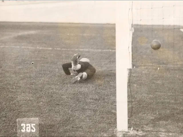 The image shows a black and white photo of a soccer player catching a ball in front of a goal post...