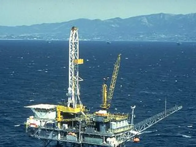 The image shows an oil rig in the middle of the ocean, surrounded by a vast expanse of blue water....