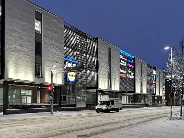 The image shows a van driving down a snowy street at night, surrounded by buildings, street poles,...