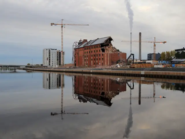 The image shows a large body of water with a factory in the background, surrounded by buildings,...