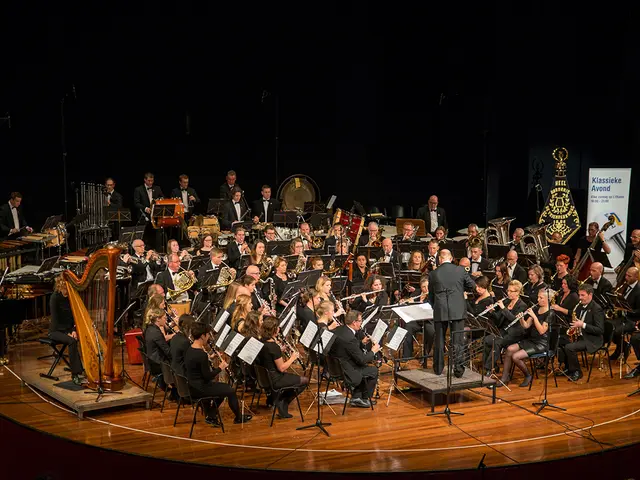 The image shows a large group of people on a stage playing musical instruments, with mics and...