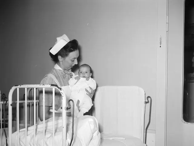 The image shows a woman in a hospital bed, cradling a baby in her arms. She is wearing a white...